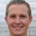 The image shows a collection of waste materials arranged on a paved driveway or courtyard area, which appears to be outside a building. The foreground features a large black plastic bin bag, partially torn, lying among several old cardboard boxes with visible corrugated fluting and some flattened toppers, indicating previous use or storage. Adjacent are a few plastic containers of various sizes, some with lids, and other miscellaneous items like crushed packaging and discarded paper. To the right, there is a noticeable stack of wooden pallets, weathered with rough textures and faded paint, positioned next to a metal trolley or cart used for transporting waste. The background reveals parts of a building wall and possibly a garage door, with natural daylight illuminating the scene. The overall setting suggests an area designated for private waste disposal or on-site rubbish clearance, aligning with services provided by Big Ben for alternative waste handling solutions outside regular municipal collection. The environment appears tidy and organized for rubbish removal activities, emphasizing the importance of proper waste segregation and disposal in sustainable projects.