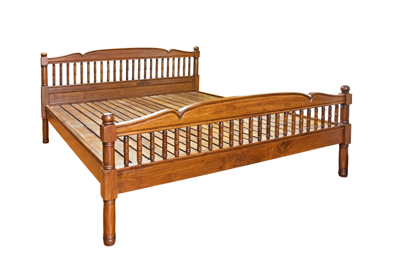 A wooden bed frame constructed from polished, medium-brown timber with a smooth finish. The frame features a headboard with vertical spindles supported by rounded posts, and a matching footboard with similar spindled detailing and rounded posts at each corner. The slatted base is visible beneath the frame, with evenly spaced wooden slats providing support. The bed is positioned against a plain white background, with no surrounding environment or additional objects visible, emphasizing the structure and craftsmanship of the wooden furniture. This detailed description focuses solely on the physical appearance and materials of the bed, aligning with the context of furniture removal or disposal in a professional waste management or rubbish removal setting, such as might be handled by Big Ben's independent collection services for bulky waste clearance or private disposal needs.